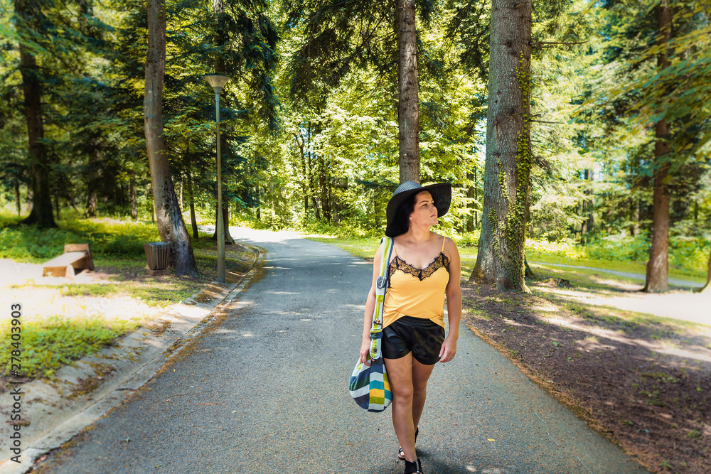 Attractive young woman with hat and bag enjoying her time outside in nature near trees Attractive young woman with hat and bag enjoying her time outside in nature near trees