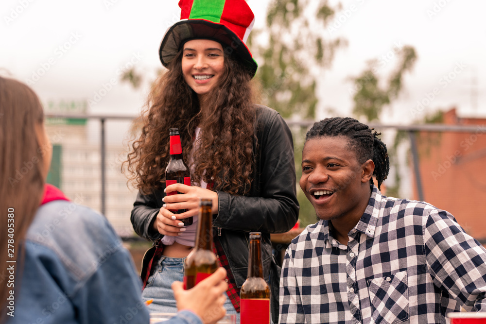 Young intercultural couple of soccer fans having beer while chatting with friend Young intercultural couple of soccer fans having beer while chatting with friend