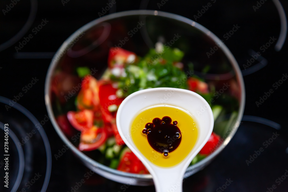 Preparation of salad from fresh vegetables, cucumbers, tomatoes and greens with a white plastic spoon containing a salad dressing made from olive oil, balsamic vinegar and soy bean sauce Preparation of salad from fresh vegetables, cucumbers, tomatoes and greens with a white plastic spoon containing a salad dressing made from olive oil, balsamic vinegar and soy bean sauce