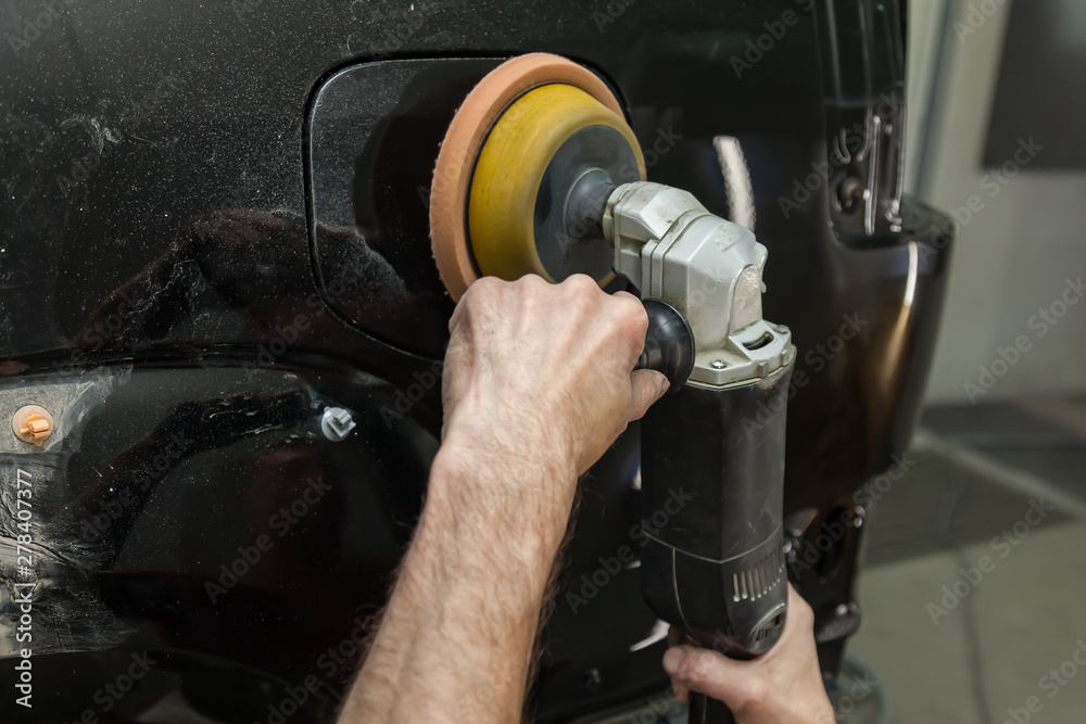 Close-up view on the hands of a male worker who holds a tool for polishing the fender of a car while working in a vehicle detailing workshop. Auto service industry. Close-up view on the hands of a male worker who holds a tool for polishing the fender of a car while working in a vehicle detailing workshop. Auto service industry.
