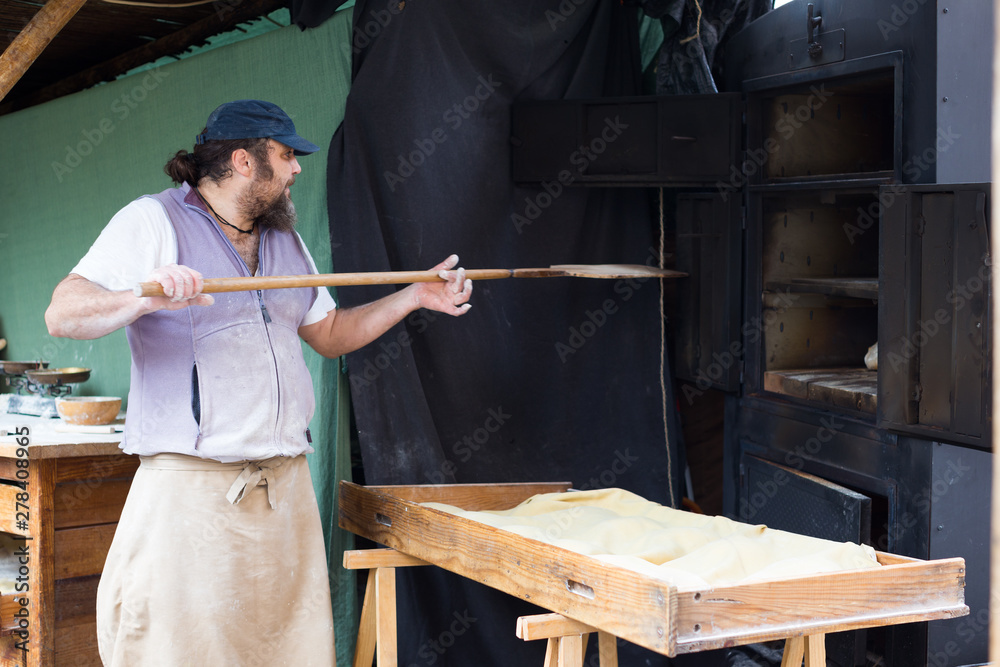 baker puts bread on the shovel into the oven baker puts bread on the shovel into the oven