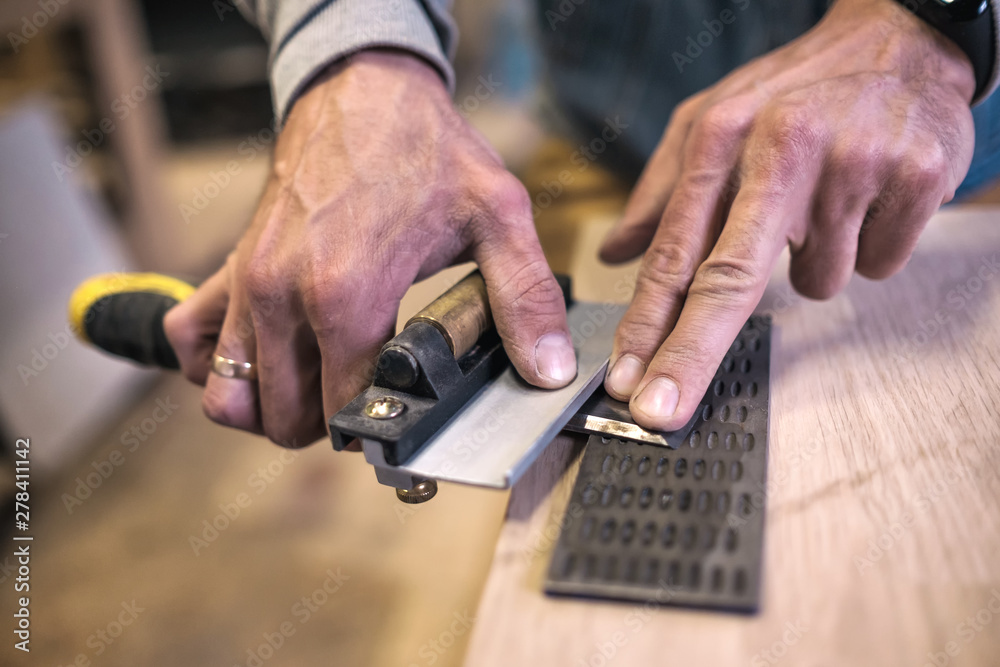 Carpenter sharpening a chisel close up view with focus on fingers
