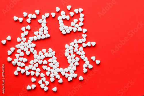 White pills in the shape of a heart on a red background. Red cross symbol. Copy space