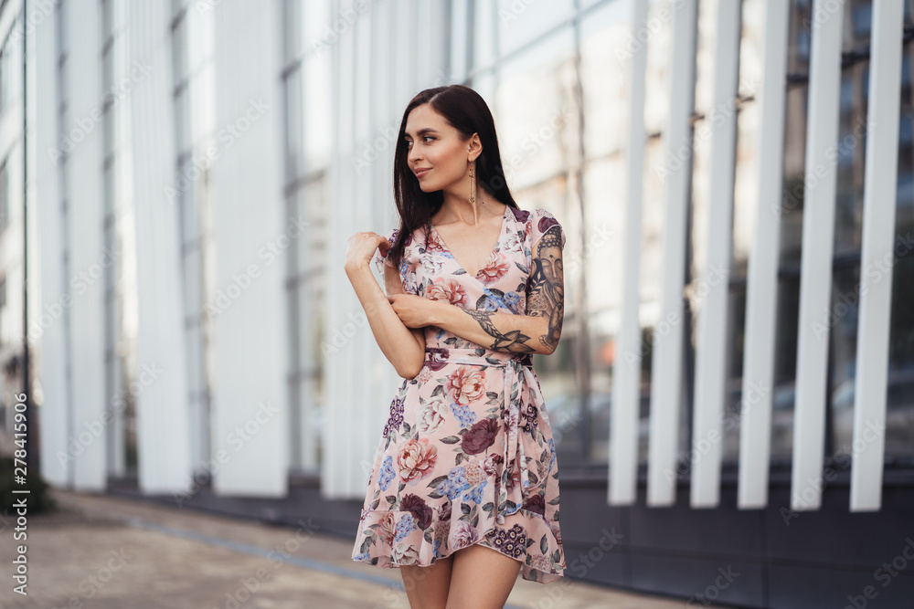 Attractive brunette girl in colored dress posing near modern building. Attractive brunette girl in colored dress posing near modern building.