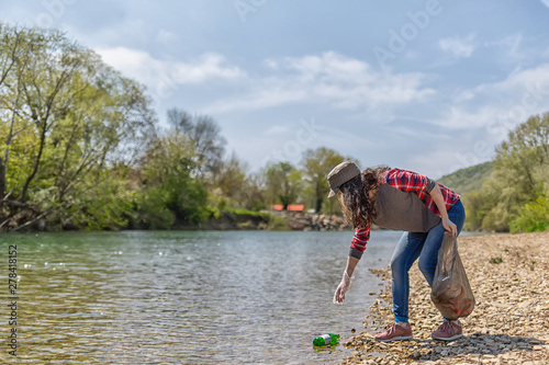 A young woman volunteer collects garbage along the river. The concept of earth day and ecology and environmental conservation. Copy space