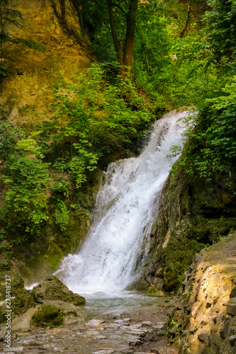 View of a small waterfall surrounded by greenery and trees.