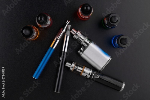 electronic cigarettes or vaping devices and bottles with vape liquid on dark background