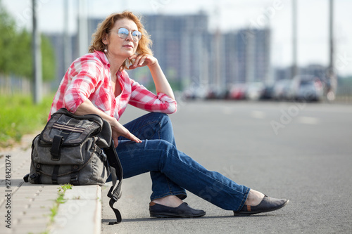 Caucasian woman hitch a ride on empty road  alone traveler sitting on roadside and waiting the car