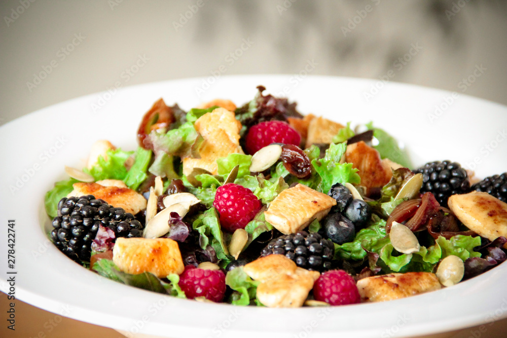 Healthy salad bowl with grilled chicken, caramelized onion and berries.