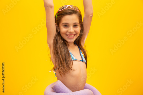 Child wearing bikini on yellow background. Concept of summer, beach and pool.