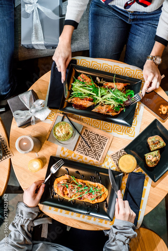 Two girls have breakfast in the restaurant. Spring rolls and grilled meat with pumpkin puree on black plates on a light wooden table in a restaurant. Flat lay. top view