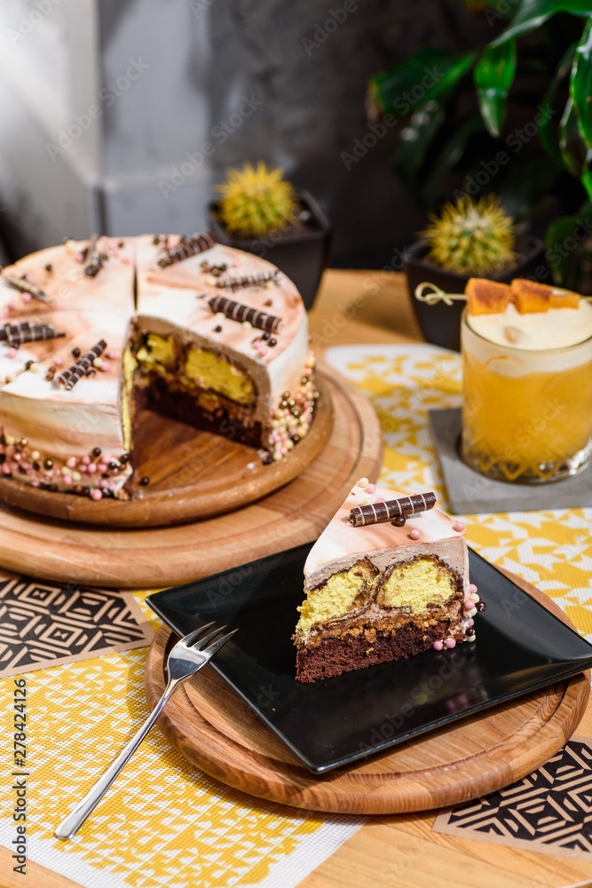 Beautiful chocolate layered cake with yellow filling and beautiful coffee glaze, decorated with tubules and pastry beads. Cake on a beautiful yellow background on a wooden table in the restaurant