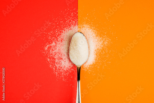 sugar with spoon on red and yellow background photo