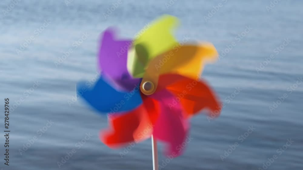 A rotate colored plastic pinwheel with a blowing wind stands on the sand by the sea against the blue smooth surface of the sea and the sunset of the day. Toy mill on the beach. Copyspace. Pattern A rotate colored plastic pinwheel with a blowing wind stands on the sand by the sea against the blue smooth surface of the sea and the sunset of the day. Toy mill on the beach. Copyspace. Pattern