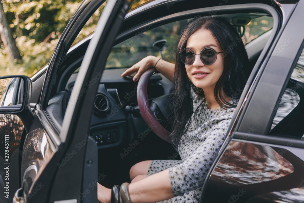 smiling pretty stylish brunette woman with sunglasses in car opens or closes the door