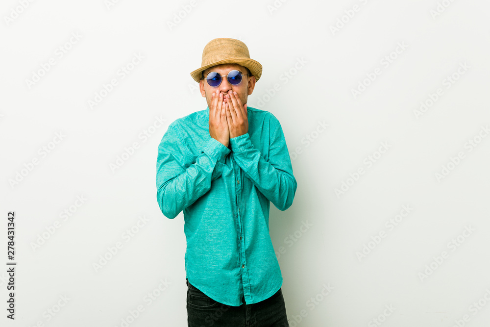 Young hispanic man wearing a summer clothes laughing about something, covering mouth with hands.