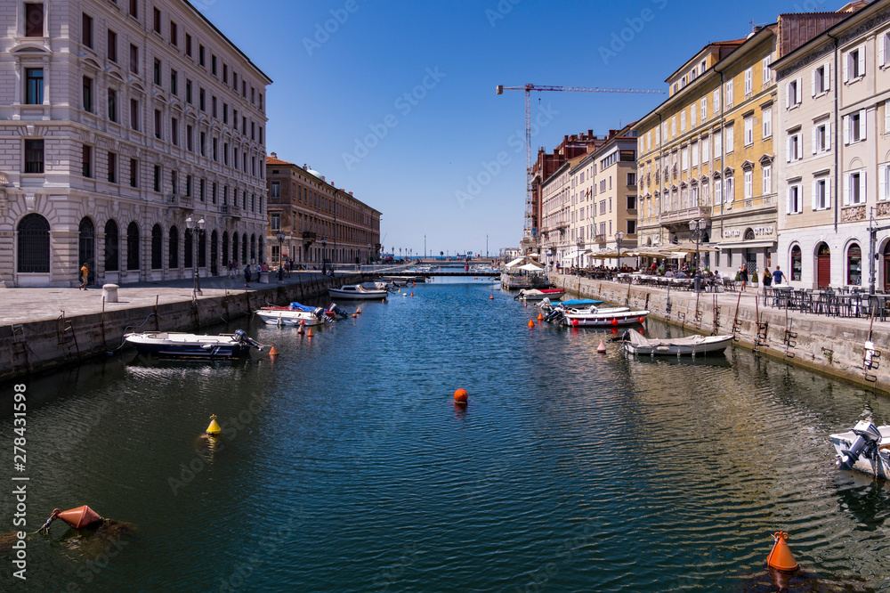 Grand Canal of Trieste with turquoise waters reflecting the buildings, with boats on both banks and in the background the Adriatic Sea, Trieste, Italy