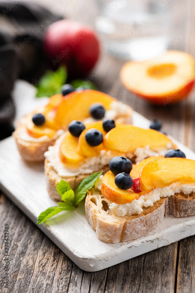 Bruschetta or appetizer toast with peach, ricotta, blueberries on wooden board. Selective focus
