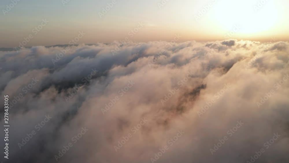 Scenic aerial view of moving white clouds. A drone flies high in the blue sky through the fluffy clouds in the evening in the bright sun. The sun is hidden behind the clouds at sunset behind the fog Scenic aerial view of moving white clouds. A drone flies high in the blue sky through the fluffy clouds in the evening in the bright sun. The sun is hidden behind the clouds at sunset behind the fog