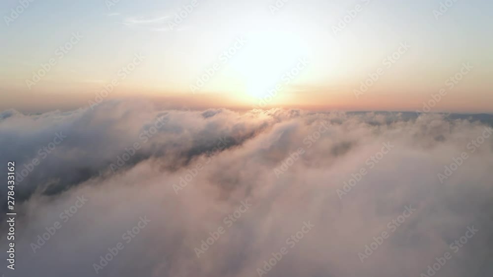 Scenic aerial view of moving white clouds. A drone flies high in the blue sky through the fluffy clouds in the evening in the bright sun. The sun is hidden behind the clouds at sunset behind the fog Scenic aerial view of moving white clouds. A drone flies high in the blue sky through the fluffy clouds in the evening in the bright sun. The sun is hidden behind the clouds at sunset behind the fog