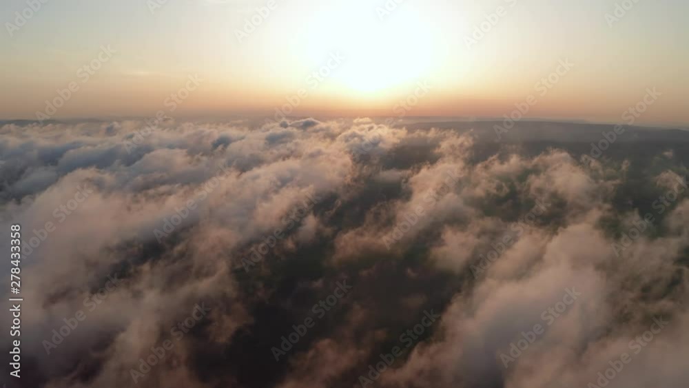 Scenic aerial view of moving white clouds. The drone flies high back in the blue sky through the fluffy clouds in the evening at the bright sun. The sun is hidden behind the clouds at sunset fog Scenic aerial view of moving white clouds. The drone flies high back in the blue sky through the fluffy clouds in the evening at the bright sun. The sun is hidden behind the clouds at sunset fog