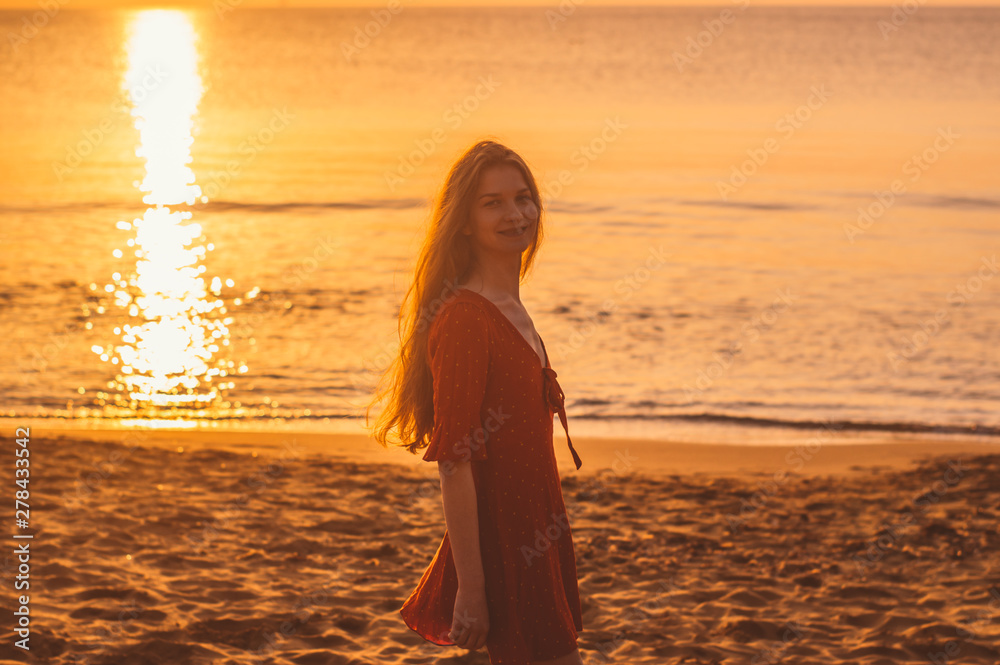 Young blonde girl in red dress staying in the evening on the beach
