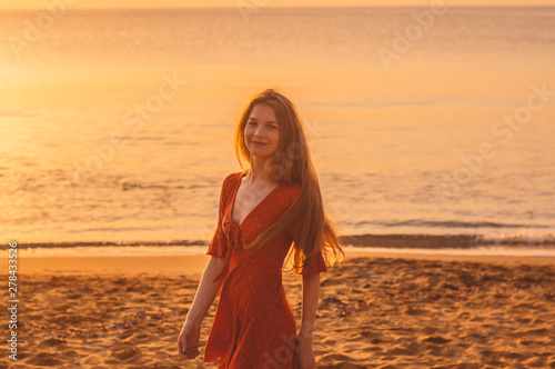 Young blonde girl in red dress walking in the evening on the beach