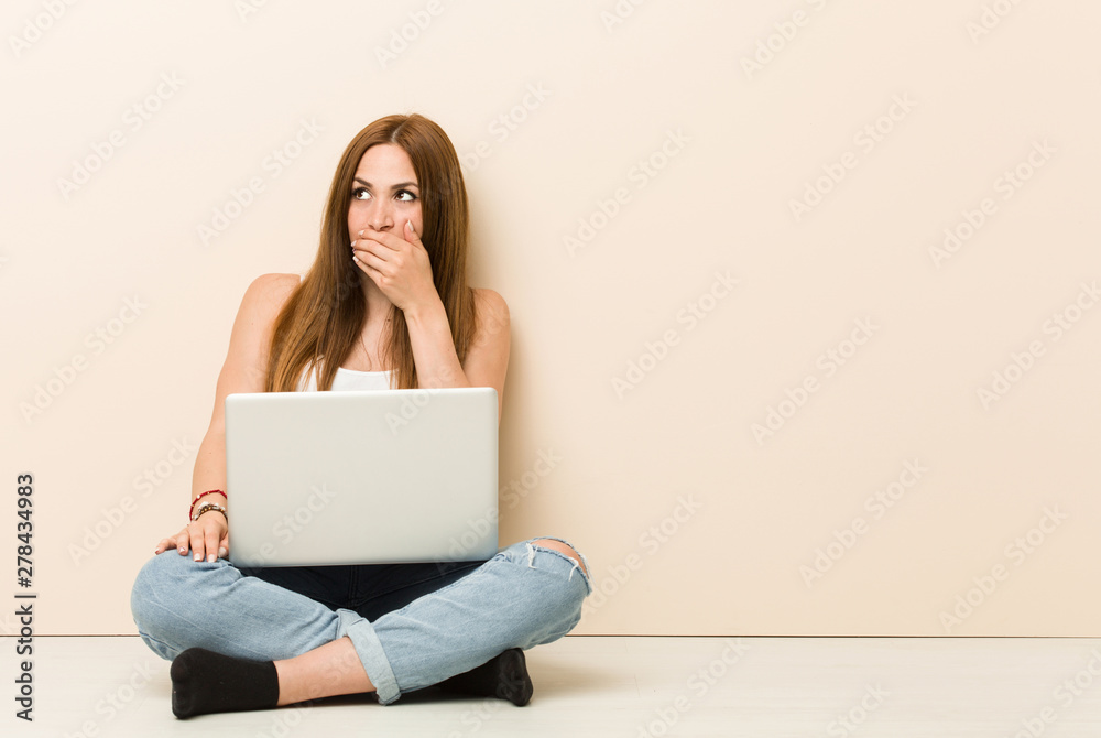 Young ginger woman sitting on her house floor thoughtful looking to a copy space covering mouth with hand. Young ginger woman sitting on her house floor thoughtful looking to a copy space covering mouth with hand.