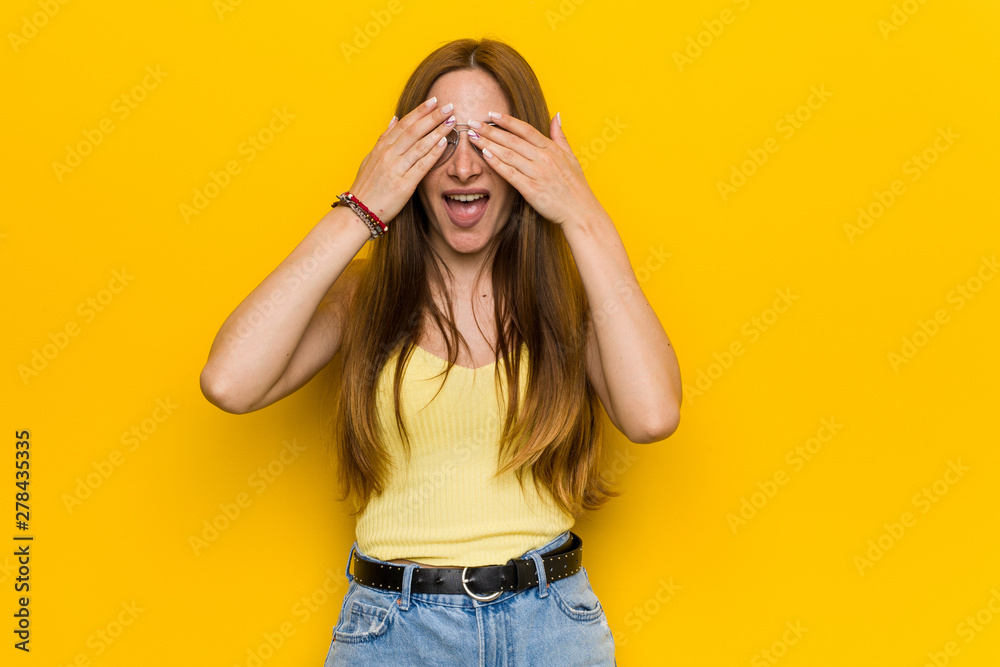 Young redhead ginger woman with freckless covers eyes with hands, smiles broadly waiting for a surprise. Young redhead ginger woman with freckless covers eyes with hands, smiles broadly waiting for a surprise.