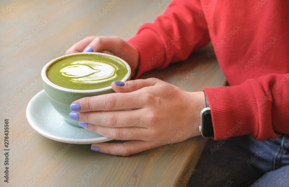 A woman in a cafe drinking a green matcha latte with vegan vegetable milk