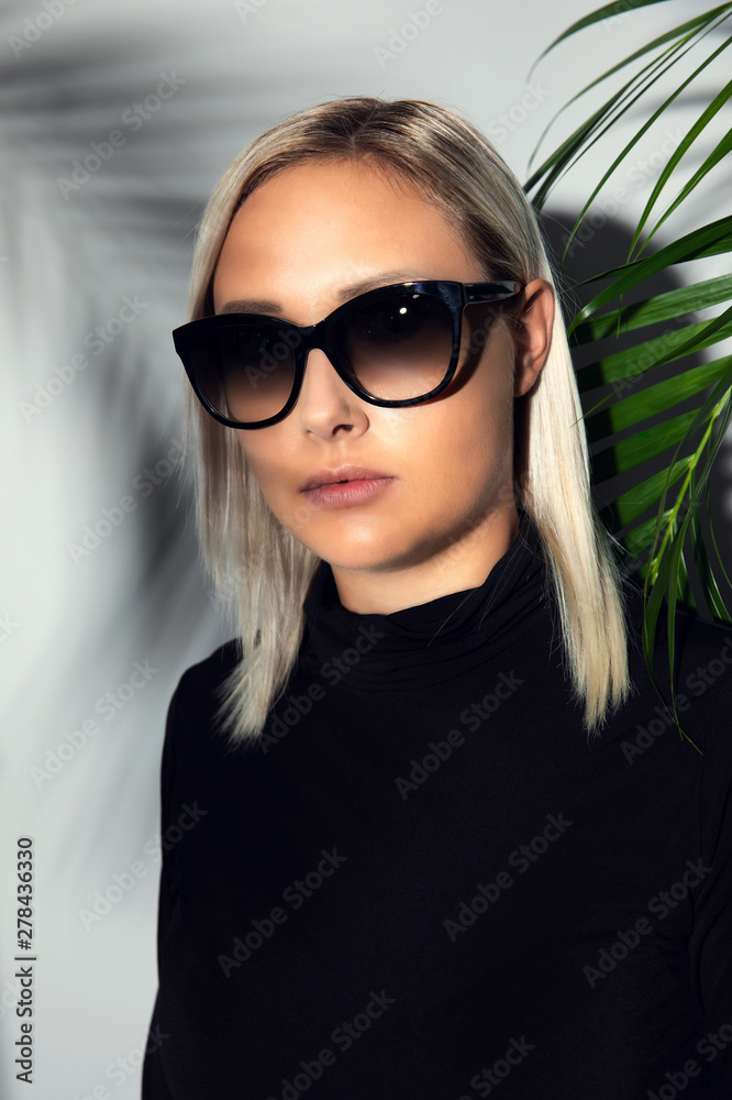 Naklejka premium Close-up of woman with sunglasses hiding behind tropical palm leaves