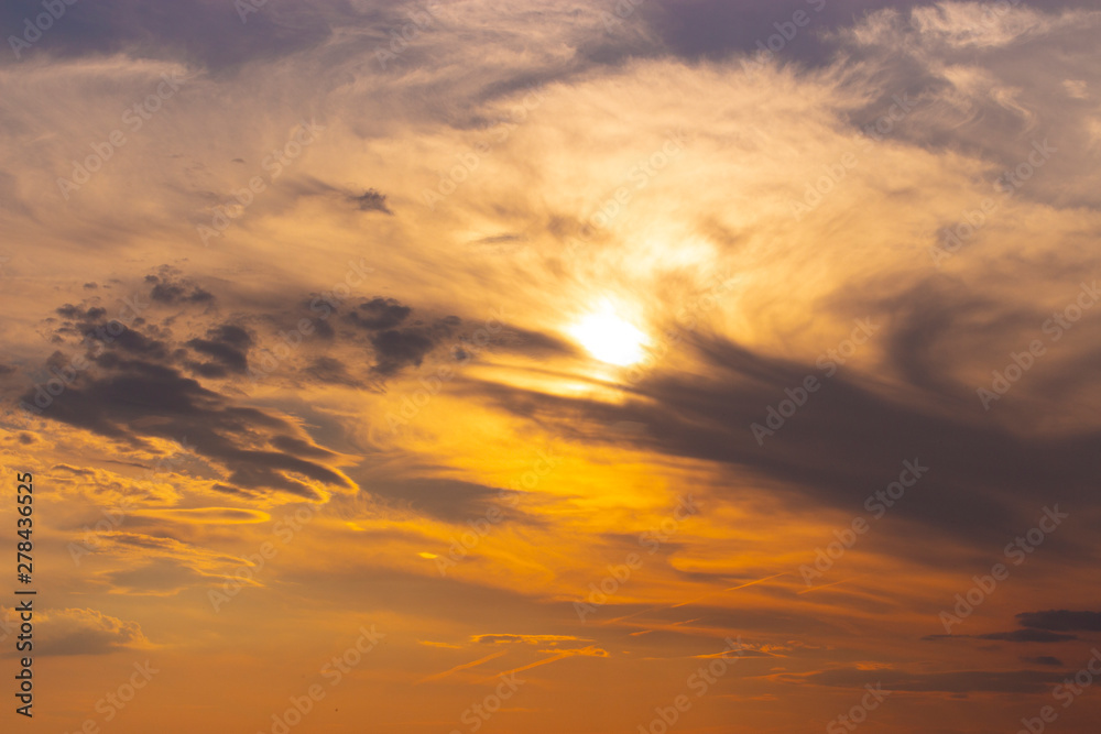 The sunset sky, the sun in the orange sky is hiding behind dark blue clouds. Beautiful sky at sunset, background wallpaper