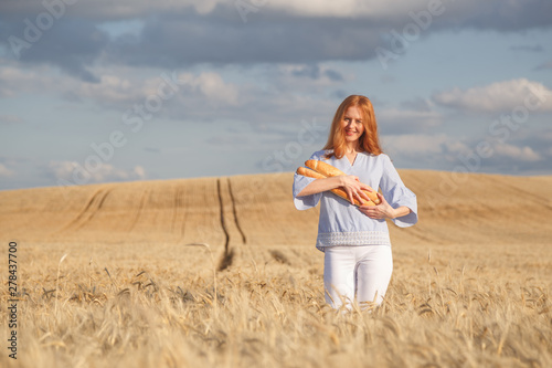 Redhead woman with two french loaves in ripe wheat field