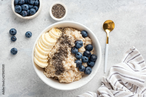 Leinwand Poster Breakfast oatmeal porridge with banana, blueberries, chia seeds on grey concrete background