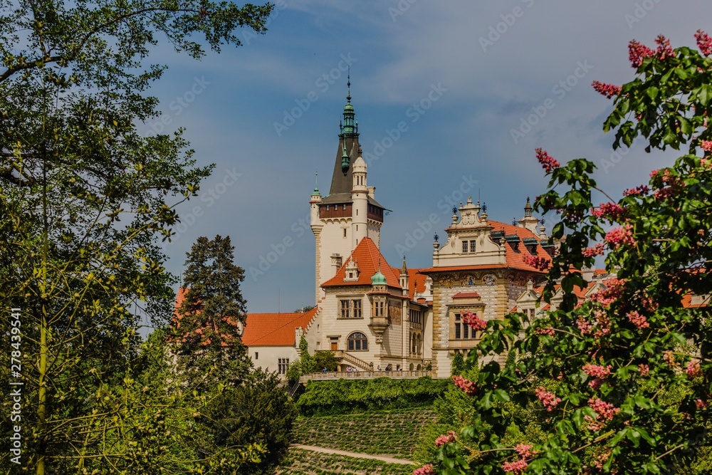 Spring view of romantic Pruhonice castle, Czech Republic, Europe, standing on hill in a park, sunny spring day with blue sky. Blooming chestnut tree in foreground. Leaves framing picture.