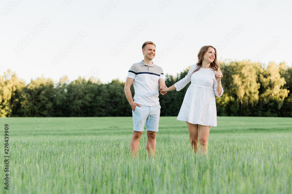 Young pretty couple in love standing in the field. Handsome cheerful blonde girl in white dress hugging her boyfriend. Man and woman having fun outdoors Young pretty couple in love standing in the field. Handsome cheerful blonde girl in white dress hugging her boyfriend. Man and woman having fun outdoors