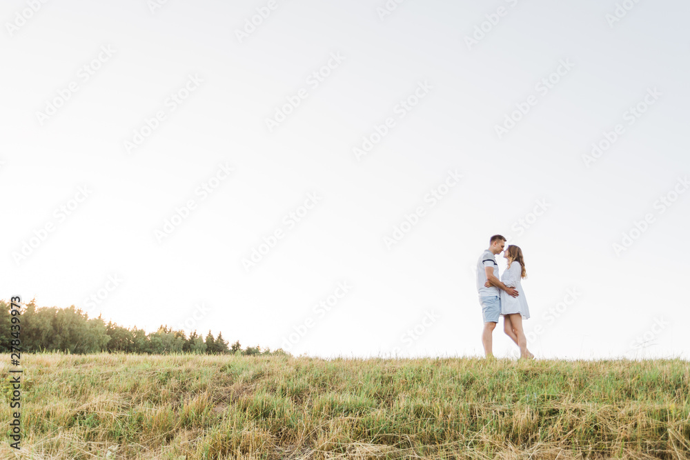 Young pretty couple in love standing in the field. Handsome cheerful blonde girl in white dress hugging her boyfriend. Man and woman having fun outdoors Young pretty couple in love standing in the field. Handsome cheerful blonde girl in white dress hugging her boyfriend. Man and woman having fun outdoors