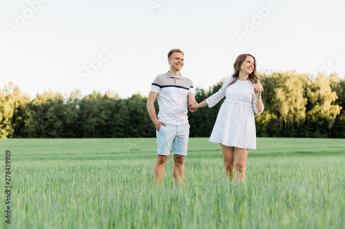 Young pretty couple in love standing in the field. Handsome cheerful blonde girl in white dress hugging her boyfriend. Man and woman having fun outdoors