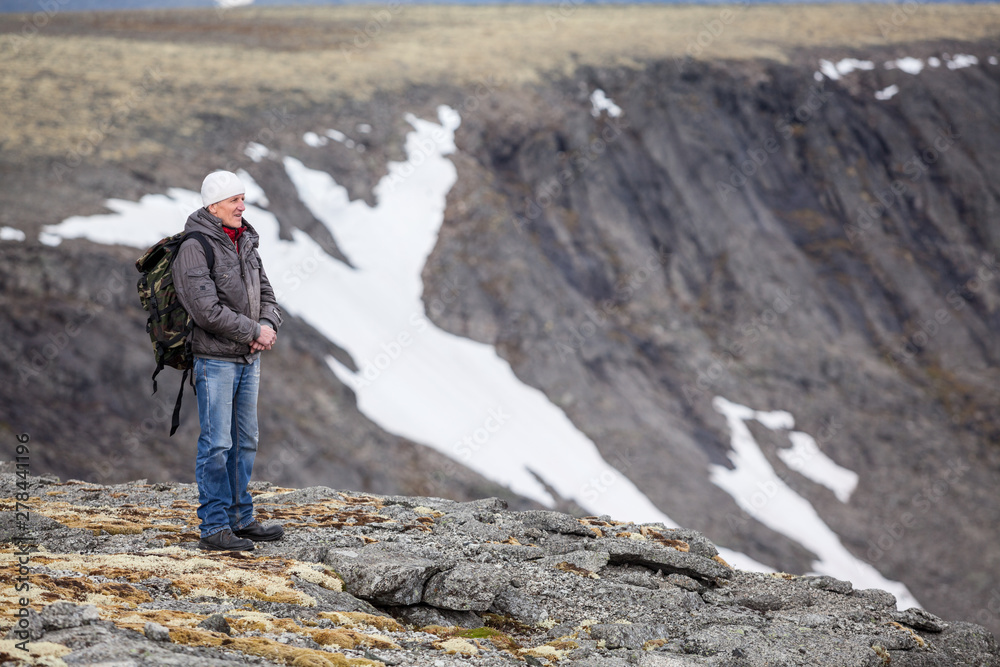 Mature Caucasian man mountain tourist standing on cliff and looking on stone valley, copy space