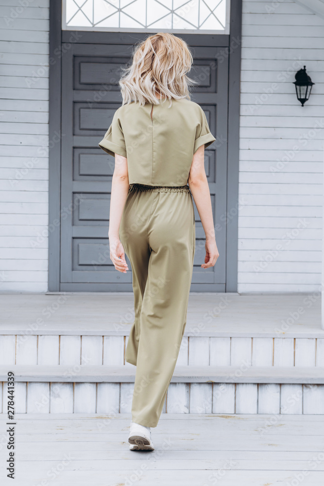 Portrait of an attractive blonde woman poses for the advertisement of a women's clothing store dressed in a olive trouser suit on the backyard of a country house