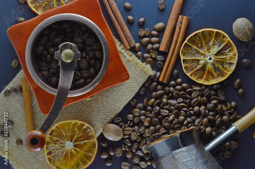 Fototapeta Naklejka Na Ścianę i Meble -  Coffee beans and a manual coffee grinder on a dark blue background, with cinnamon sticks and orange slices
