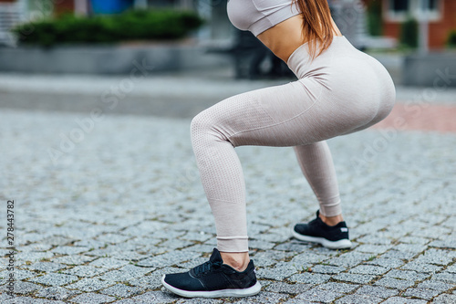 Photo of the back, sexy ass, girl doing squats, before physical workout on the street in the city.