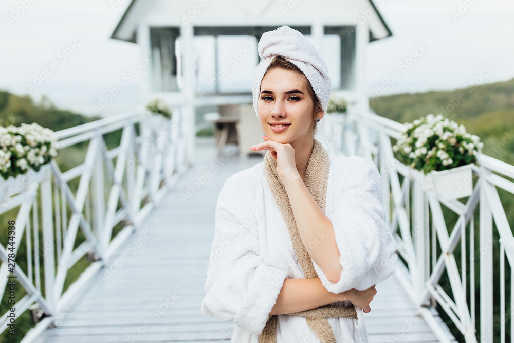 Portrait of pretty, young woman resting in luxury resort in mountains, stay on villa terrace and posing, wearing at white robe.