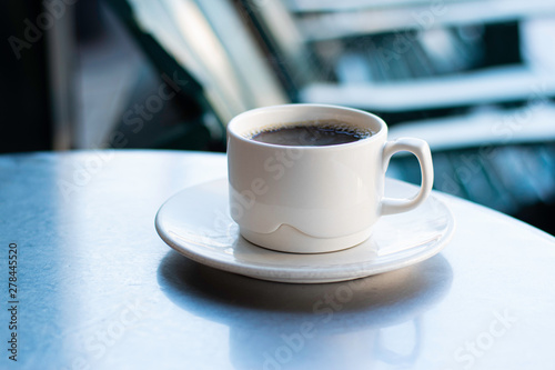 Black Coffee in White Cup on Saucer on metal table outside with reflections and steam