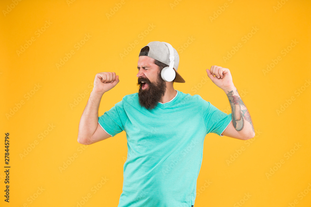 Modern and popular. Bearded man enjoying modern music on yellow background. Modern hipster in stylish headphones listening and singing to modern song. Using modern technology for pleasure Modern and popular. Bearded man enjoying modern music on yellow background. Modern hipster in stylish headphones listening and singing to modern song. Using modern technology for pleasure