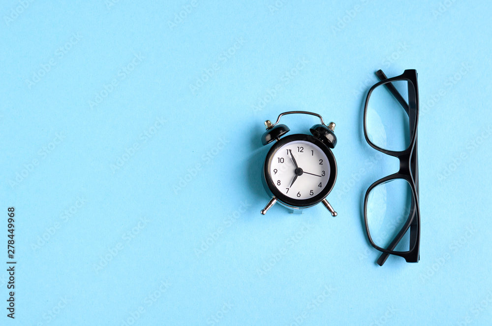 Black glasses and alarm clock on blue background composition. Black glasses and alarm clock on blue background composition.