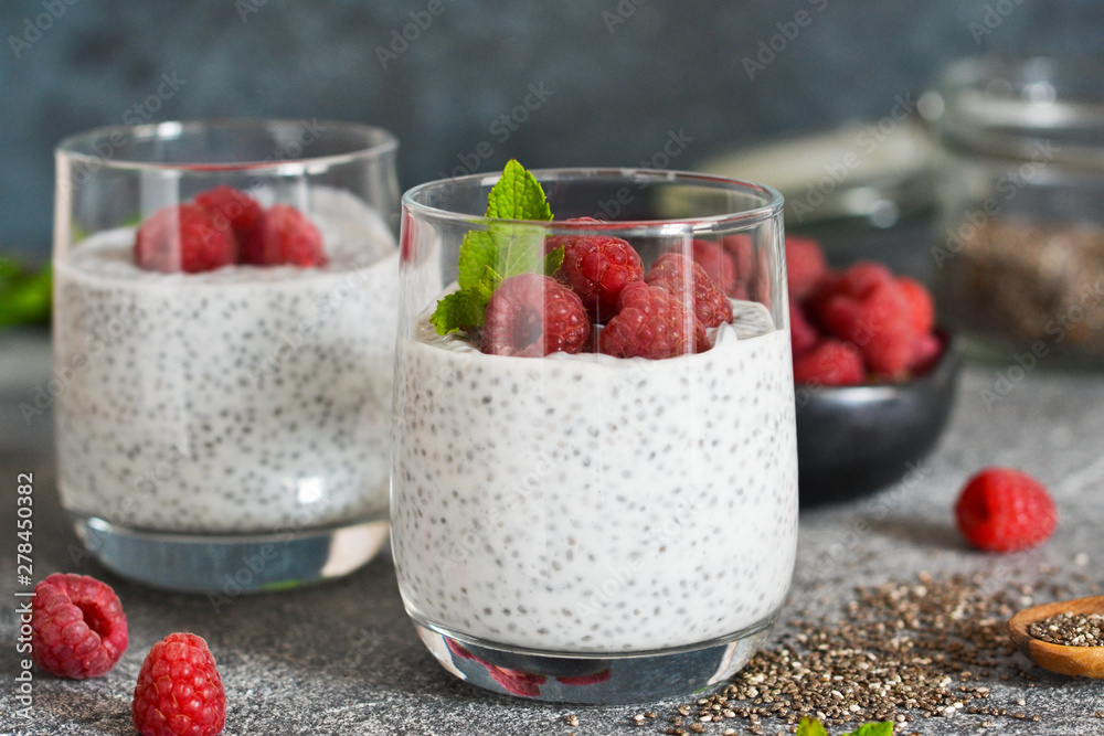 Chia pudding with yogurt and raspberries in a glass on concrete background Chia pudding with yogurt and raspberries in a glass on concrete background