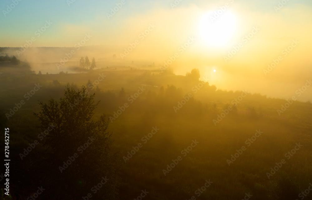 Orange sunny light with rays and shadows over the foggy river at dawn. The fog rises above water and stretches to the rising sun. Sunlit misty forest and river in nature Orange sunny light with rays and shadows over the foggy river at dawn. The fog rises above water and stretches to the rising sun. Sunlit misty forest and river in nature