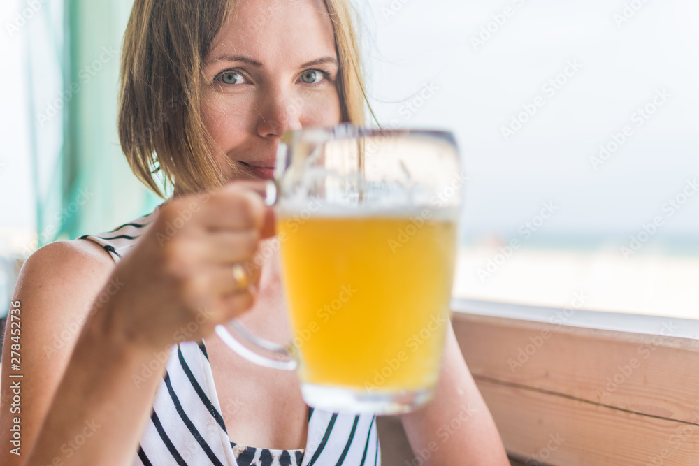 A contented smiling woman is holding a glass of cold beer in the summer on a terrace at a restaurant table. A contented smiling woman is holding a glass of cold beer in the summer on a terrace at a restaurant table.