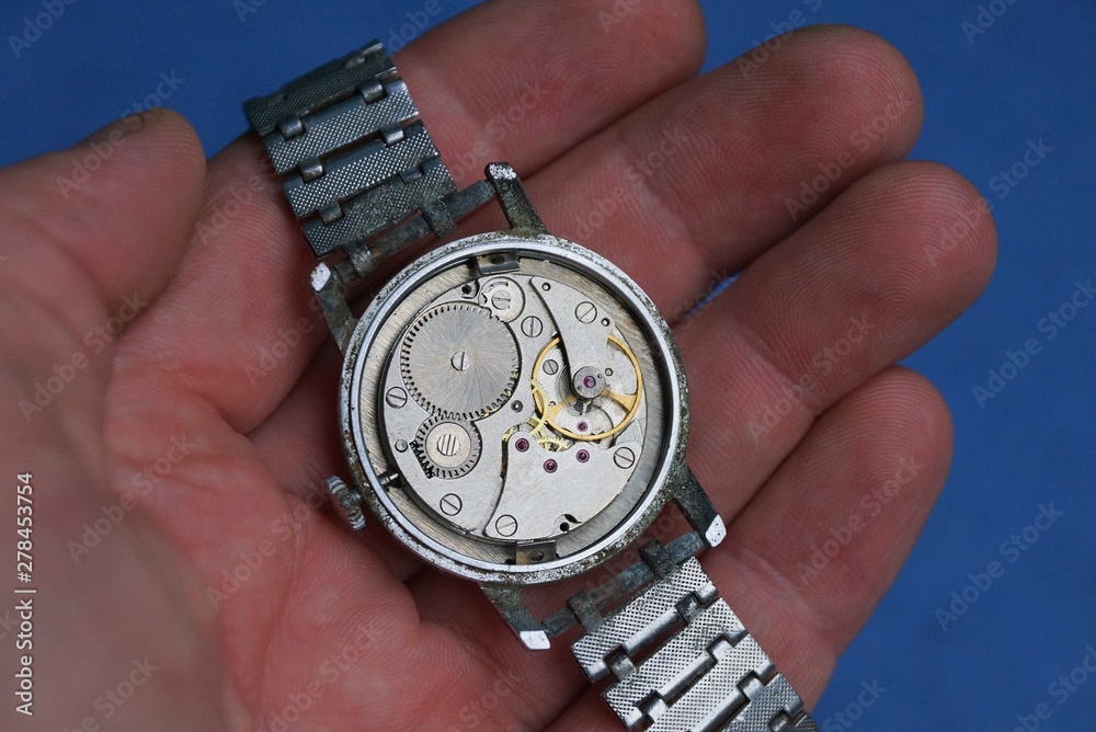 open old gray clock on fingers on blue background open old gray clock on fingers on blue background
